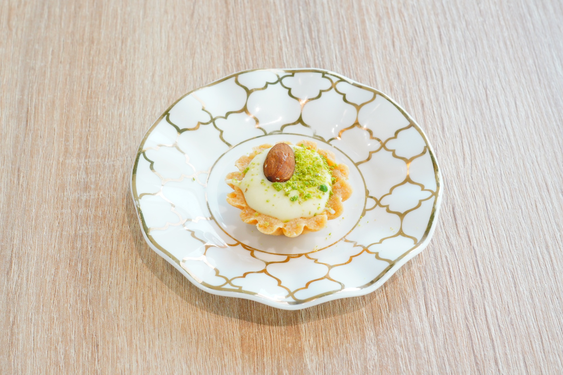 Mini tart with cream, crushed pistachio and a whole almond