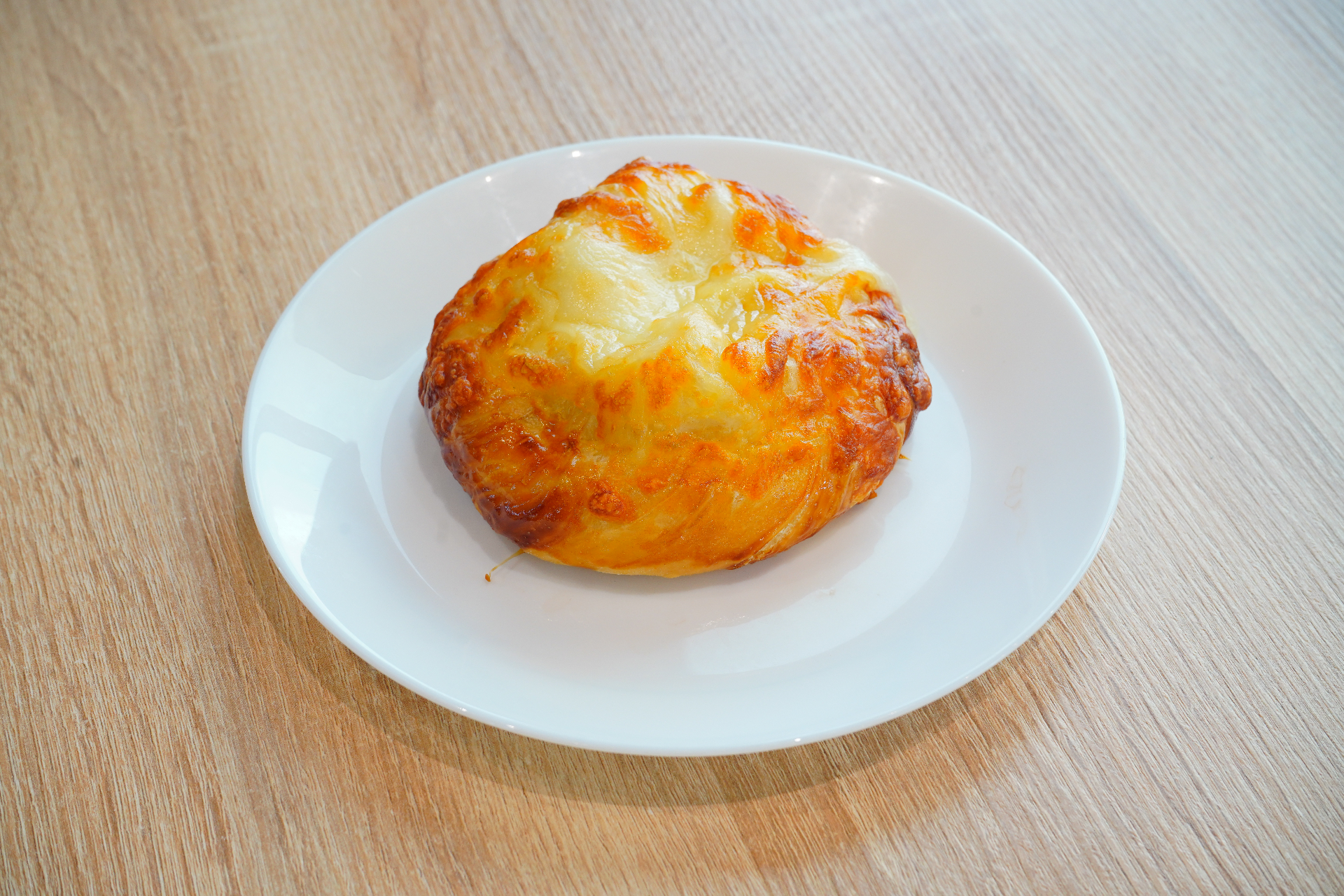 Golden cheese-topped pogaca on a white plate